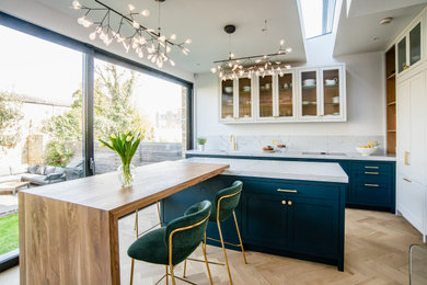 Inspiration for a large traditional l-shaped kitchen/diner in London with a built-in sink, shaker cabinets, blue cabinets, engineered stone countertops, white splashback, engineered quartz splashback, black appliances, light hardwood flooring, an island, brown floors and white worktops.