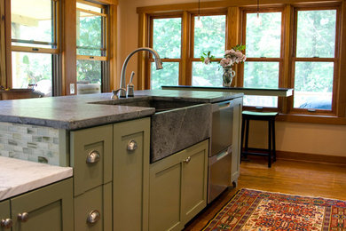 Photo of a country kitchen in DC Metro with a farmhouse sink, green cabinets, soapstone benchtops, glass tile splashback and light hardwood floors.