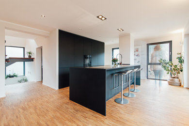 Offene, Zweizeilige, Mittelgroße Moderne Küche mit Unterbauwaschbecken, flächenbündigen Schrankfronten, schwarzen Schränken, Laminat-Arbeitsplatte, schwarzen Elektrogeräten, braunem Holzboden, Kücheninsel, schwarzer Arbeitsplatte und eingelassener Decke in Sonstige