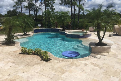 Photo of a large tropical backyard custom-shaped lap pool in Orlando with a hot tub and natural stone pavers.