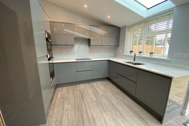 Inspiration for a medium sized contemporary grey and brown u-shaped open plan kitchen in Other with an integrated sink, flat-panel cabinets, grey cabinets, composite countertops, white splashback, integrated appliances, vinyl flooring, no island, brown floors, white worktops, a vaulted ceiling and feature lighting.