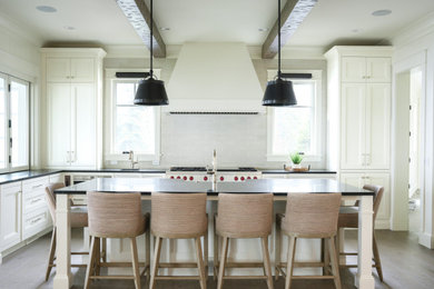 Example of a large beach style l-shaped medium tone wood floor, brown floor and exposed beam eat-in kitchen design in Detroit with a farmhouse sink, recessed-panel cabinets, white cabinets, soapstone countertops, white backsplash, ceramic backsplash, paneled appliances, an island and black countertops