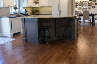 Mid-sized transitional l-shaped dark wood floor and brown floor eat-in kitchen photo in Minneapolis with an undermount sink, shaker cabinets, white cabinets, granite countertops, gray backsplash, subway tile backsplash, paneled appliances and an island