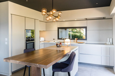 Photo of a medium sized modern l-shaped open plan kitchen in Grenoble with a single-bowl sink, flat-panel cabinets, white cabinets, laminate countertops, white splashback, integrated appliances, an island, grey floors and white worktops.
