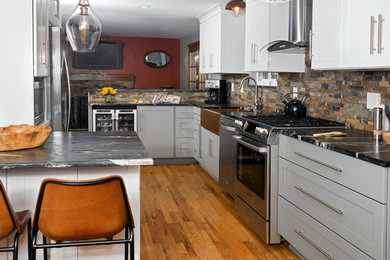 This is an example of a mid-sized transitional u-shaped eat-in kitchen in Other with a farmhouse sink, shaker cabinets, grey cabinets, marble benchtops, multi-coloured splashback, stone tile splashback, stainless steel appliances, medium hardwood floors, a peninsula, beige floor and black benchtop.