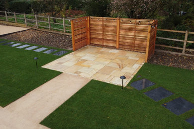 Inspiration for a large modern back formal full sun garden for summer in West Midlands with lawn edging, natural stone paving and a wood fence.