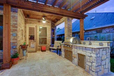 This is an example of a mid-sized country backyard patio with an outdoor kitchen, natural stone pavers and a pergola.