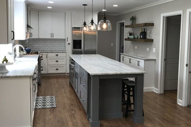 Example of a mid-sized cottage l-shaped dark wood floor and brown floor open concept kitchen design in Chicago with a farmhouse sink, shaker cabinets, white cabinets, granite countertops, white backsplash, subway tile backsplash, stainless steel appliances and an island