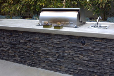 Example of a large island style backyard stone patio kitchen design in San Diego with no cover
