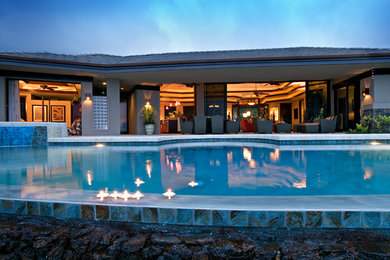 This is an example of a large tropical backyard custom-shaped pool in Hawaii with a hot tub and natural stone pavers.