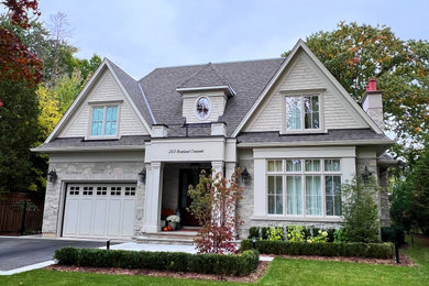 This is an example of a large transitional two-storey beige house exterior in Toronto with stone veneer, a gable roof, a shingle roof, a brown roof and shingle siding.