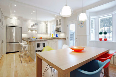 Inspiration for a mid-sized transitional u-shaped light wood floor and beige floor eat-in kitchen remodel in Toronto with raised-panel cabinets, white cabinets, granite countertops, white backsplash, an island, an undermount sink, ceramic backsplash and stainless steel appliances