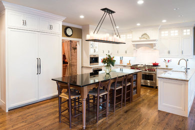 This is an example of a large traditional l-shaped eat-in kitchen in Wilmington with a farmhouse sink, beaded inset cabinets, white cabinets, marble benchtops, white splashback, subway tile splashback, stainless steel appliances, medium hardwood floors, with island and brown floor.