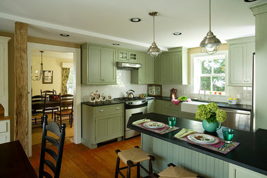 Example of a mid-sized classic u-shaped medium tone wood floor eat-in kitchen design in Jacksonville with a farmhouse sink, recessed-panel cabinets, green cabinets, soapstone countertops, white backsplash, ceramic backsplash, stainless steel appliances and black countertops