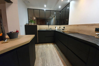 Exemple d'une cuisine ouverte moderne en U de taille moyenne avec un évier encastré, un placard à porte plane, des portes de placard noires, un plan de travail en stratifié, une crédence en bois, un électroménager noir, parquet clair, îlot et plan de travail noir.
