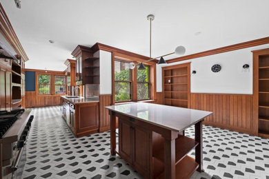 This is an example of a large galley kitchen/diner in New York with a built-in sink, recessed-panel cabinets, medium wood cabinets, engineered stone countertops, integrated appliances, ceramic flooring, an island, multi-coloured floors and white worktops.