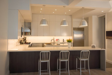Large trendy u-shaped light wood floor open concept kitchen photo in New York with an undermount sink, shaker cabinets, white cabinets, quartz countertops, white backsplash, ceramic backsplash, stainless steel appliances and an island