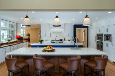 Kitchen - huge transitional u-shaped brown floor kitchen idea in Boston with a farmhouse sink, shaker cabinets, quartz countertops, white backsplash, quartz backsplash, stainless steel appliances, two islands and white countertops