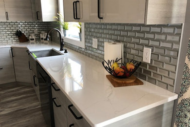 Inspiration for a large contemporary l-shaped kitchen/diner in Grand Rapids with a belfast sink, flat-panel cabinets, grey cabinets, marble worktops, metallic splashback, porcelain flooring, an island, grey floors, white worktops, glass tiled splashback and stainless steel appliances.