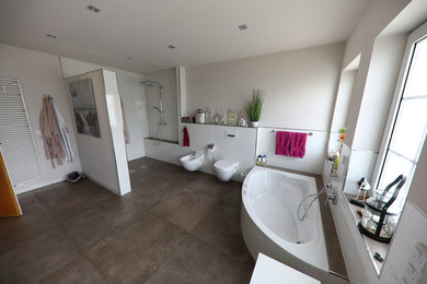 Großes Modernes Duschbad mit flächenbündigen Schrankfronten, weißen Schränken, Whirlpool, bodengleicher Dusche, Wandtoilette mit Spülkasten, weißen Fliesen, Keramikfliesen, beiger Wandfarbe, Keramikboden, Aufsatzwaschbecken, Mineralwerkstoff-Waschtisch, braunem Boden, offener Dusche und weißer Waschtischplatte in Düsseldorf