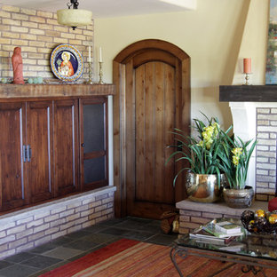 Ejemplo de salón para visitas abierto, mediterráneo, grande, con paredes beige, suelo de pizarra, chimenea tradicional, marco de chimenea de ladrillo y televisor retractable