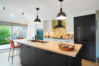 Inspiration for a large contemporary galley open concept kitchen remodel in Denver with an undermount sink, flat-panel cabinets, white cabinets, yellow backsplash, black appliances and an island