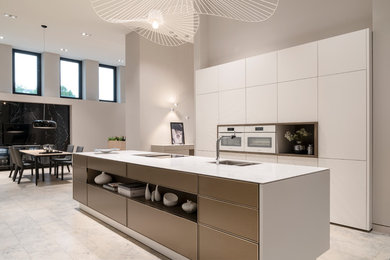 Offene, Einzeilige, Große Moderne Küche mit Einbauwaschbecken, flächenbündigen Schrankfronten, grauen Schränken, Mineralwerkstoff-Arbeitsplatte, Küchenrückwand in Grau, schwarzen Elektrogeräten, Marmorboden, Kücheninsel, beigem Boden und schwarzer Arbeitsplatte in Köln