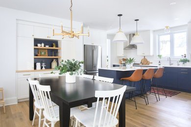 Mid-sized transitional open plan dining in Toronto with white walls, light hardwood floors, a standard fireplace, a wood fireplace surround and brown floor.