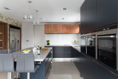 Inspiration for a mid-sized contemporary l-shaped eat-in kitchen in London with an integrated sink, flat-panel cabinets, blue cabinets, quartzite benchtops, white splashback, glass sheet splashback, panelled appliances, porcelain floors and with island.