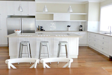 This is an example of a large transitional l-shaped eat-in kitchen in Sydney with an undermount sink, shaker cabinets, white cabinets, quartz benchtops, white splashback, subway tile splashback, stainless steel appliances, medium hardwood floors and with island.