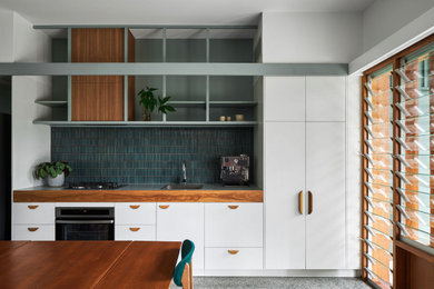 Design ideas for a small tropical single-wall kitchen in Brisbane with an integrated sink, white cabinets, laminate benchtops, green splashback, ceramic splashback, stainless steel appliances, concrete floors, no island, grey floor and green benchtop.
