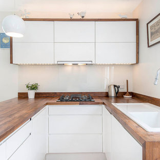 Diseño de cocina en U, actual, con fregadero encastrado, armarios con paneles lisos, puertas de armario blancas, encimera de madera, salpicadero blanco, salpicadero de vidrio templado y península