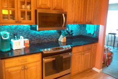 Eat-in kitchen - mid-sized traditional u-shaped light wood floor eat-in kitchen idea in Boston with an undermount sink, raised-panel cabinets, medium tone wood cabinets, granite countertops, black backsplash, glass tile backsplash, stainless steel appliances and an island