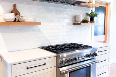 Example of a large cottage light wood floor eat-in kitchen design in Portland Maine with shaker cabinets, white cabinets, white backsplash, subway tile backsplash, stainless steel appliances, white countertops, a single-bowl sink and an island