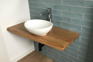 Kleines Landhaus Badezimmer mit grünen Fliesen, Porzellanfliesen, grüner Wandfarbe, Laminat, Aufsatzwaschbecken, Waschtisch aus Holz, braunem Boden, brauner Waschtischplatte, Einzelwaschbecken und schwebendem Waschtisch