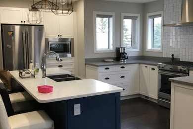 Inspiration for a mid-sized transitional u-shaped dark wood floor and brown floor kitchen remodel in Other with a farmhouse sink, shaker cabinets, white cabinets, quartzite countertops, white backsplash, subway tile backsplash, stainless steel appliances, an island and gray countertops