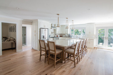 Eat-in kitchen - mid-sized transitional l-shaped light wood floor eat-in kitchen idea with a farmhouse sink, shaker cabinets, white cabinets, quartzite countertops, white backsplash, subway tile backsplash, stainless steel appliances, an island and beige countertops