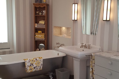 Large traditional kids bathroom in Other with furniture-like cabinets, a freestanding tub, an alcove shower, a wall-mount toilet, gray tile, stone tile, grey walls, medium hardwood floors, a pedestal sink, marble benchtops, brown floor and a hinged shower door.