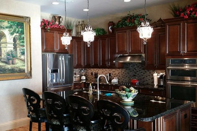 Example of a small classic l-shaped light wood floor and beige floor open concept kitchen design in Miami with a double-bowl sink, raised-panel cabinets, dark wood cabinets, granite countertops, multicolored backsplash, glass tile backsplash, stainless steel appliances and an island