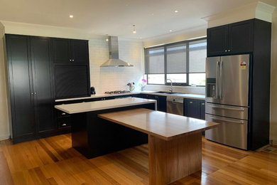 Inspiration for a large contemporary l-shaped open plan kitchen in Melbourne with shaker cabinets, with island, a double-bowl sink, black cabinets, granite benchtops, white splashback, porcelain splashback, stainless steel appliances, white benchtop and medium hardwood floors.