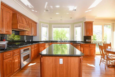 Inspiration for a large timeless u-shaped light wood floor and beige floor eat-in kitchen remodel in San Francisco with raised-panel cabinets, medium tone wood cabinets, granite countertops, black backsplash, stone slab backsplash, stainless steel appliances, an island and black countertops