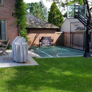Small modern backyard partial sun outdoor sport court in Toronto with with outdoor playset and concrete pavers for summer.