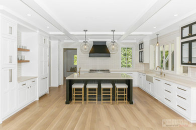 Inspiration for a large 1960s l-shaped medium tone wood floor, brown floor and exposed beam eat-in kitchen remodel with a farmhouse sink, recessed-panel cabinets, white cabinets, quartz countertops, white backsplash, subway tile backsplash, stainless steel appliances, an island and gray countertops
