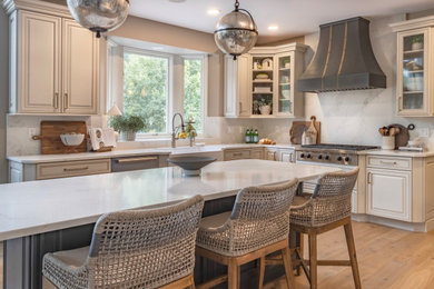Large transitional u-shaped light wood floor and brown floor eat-in kitchen photo in Detroit with a farmhouse sink, raised-panel cabinets, beige cabinets, quartz countertops, white backsplash, quartz backsplash, stainless steel appliances, an island and white countertops