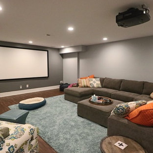 This is an example of a medium sized classic enclosed home cinema in Louisville with grey walls, medium hardwood flooring, a projector screen and brown floors.