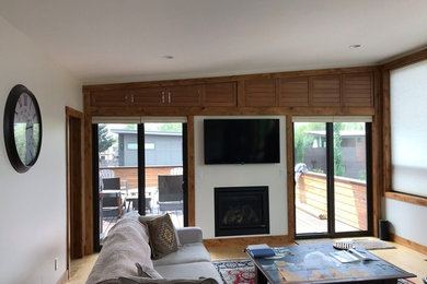 Example of a mid-sized trendy enclosed light wood floor and beige floor living room design in Other with beige walls, a standard fireplace and a wall-mounted tv