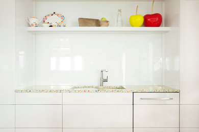 Example of a mid-sized trendy galley light wood floor enclosed kitchen design in Montreal with an undermount sink, flat-panel cabinets, white cabinets, recycled glass countertops, white backsplash, glass sheet backsplash, white appliances and no island