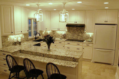 Example of a mid-sized classic u-shaped travertine floor enclosed kitchen design in St Louis with an undermount sink, raised-panel cabinets, white cabinets, granite countertops, stone slab backsplash, white appliances and a peninsula