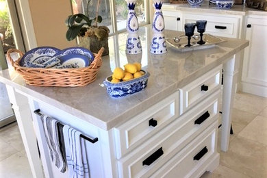 Inspiration for a large country kitchen in Los Angeles with a farmhouse sink, white cabinets, quartzite benchtops, beige splashback, porcelain splashback, stainless steel appliances, travertine floors, with island and beige floor.