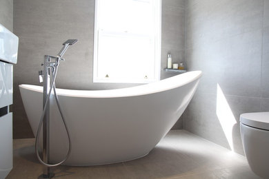 Photo of a large contemporary family bathroom in London with flat-panel cabinets, grey cabinets, a freestanding bath, a corner shower, a wall mounted toilet, grey tiles, porcelain tiles, grey walls, porcelain flooring, a wall-mounted sink, grey floors and a hinged door.